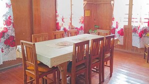 Un comedor con mesa y sillas de madera, ventanas amplias con cortinas florales y paredes de madera.