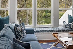 A cozy seating area with a sofa and bench, large windows with a view of a lake, and a wooden table. - Tranquil Waterfront Retreat + Sunrise Views (Bluffton)
