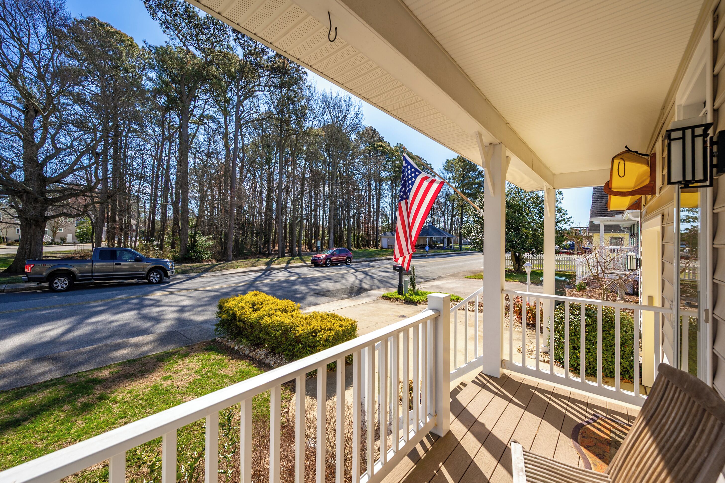 A porch with a view of a street, a flag, and a vehicle.