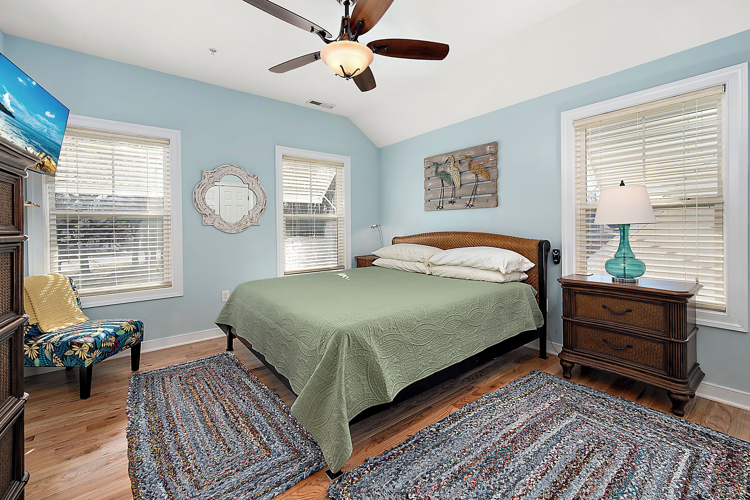 A bedroom with a bed, a chair, a nightstand, a lamp, and a ceiling fan.