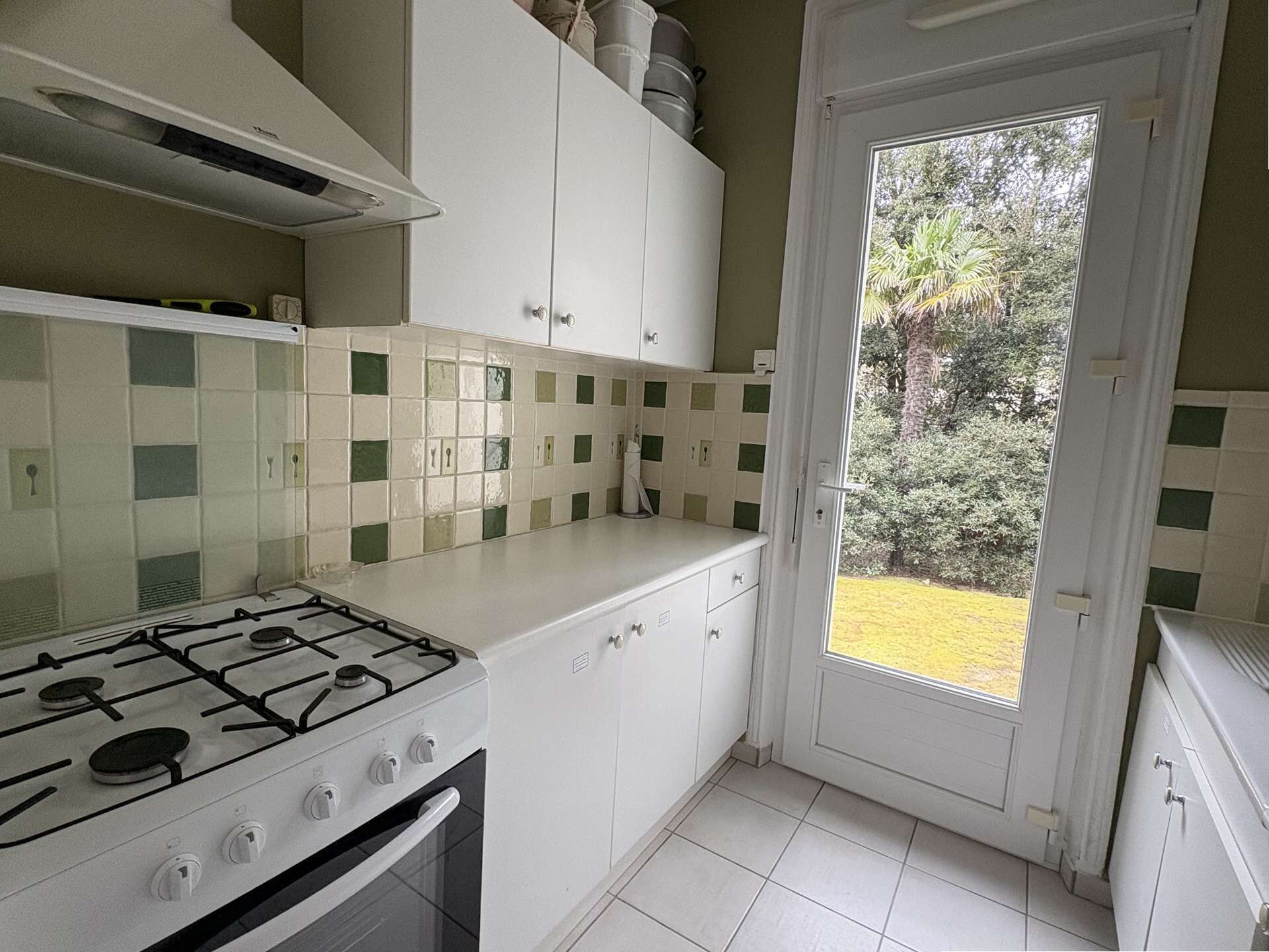 A kitchen with a gas stove, white cabinets, a tiled backsplash, and a door leading to a garden.