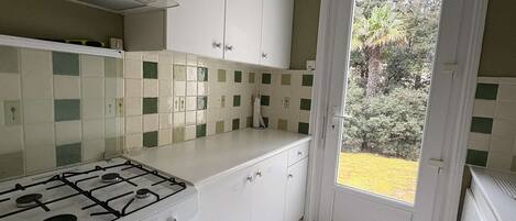 A kitchen with a gas stove, white cabinets, a tiled backsplash, and a door leading to a garden.