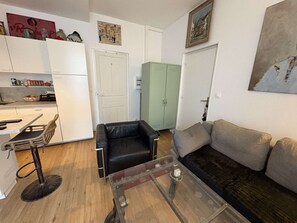A compact living space with a kitchenette, a dining area with a chair, a sofa, and a glass coffee table. - PORNICHET - PLACE DU MARCHE (PORNICHET)
