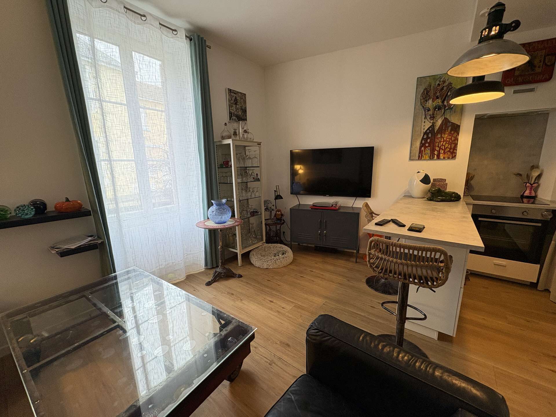 Un salon moderne comprenant une table basse avec un plateau en verre, un canapé en cuir, un téléviseur, un coin cuisine avec un four et une table à manger.