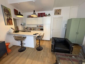 A compact kitchen with white cabinets, a central island, two bar stools, a black leather sofa, and a green wardrobe. - PORNICHET - PLACE DU MARCHE (PORNICHET)
