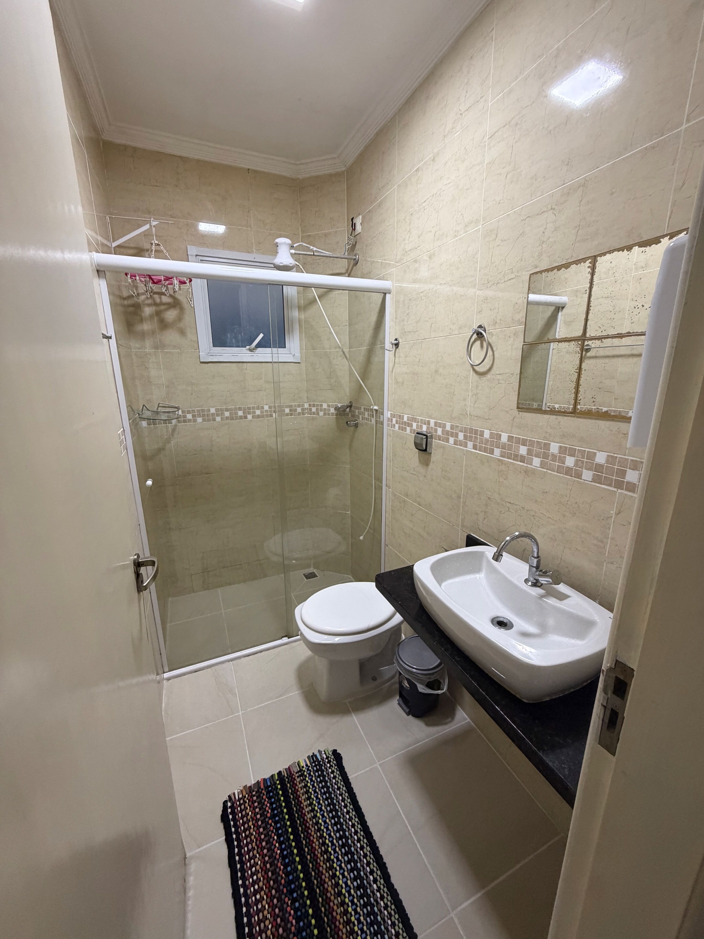 Un baño con ducha de vidrio, inodoro, lavamanos y suelo de baldosas.