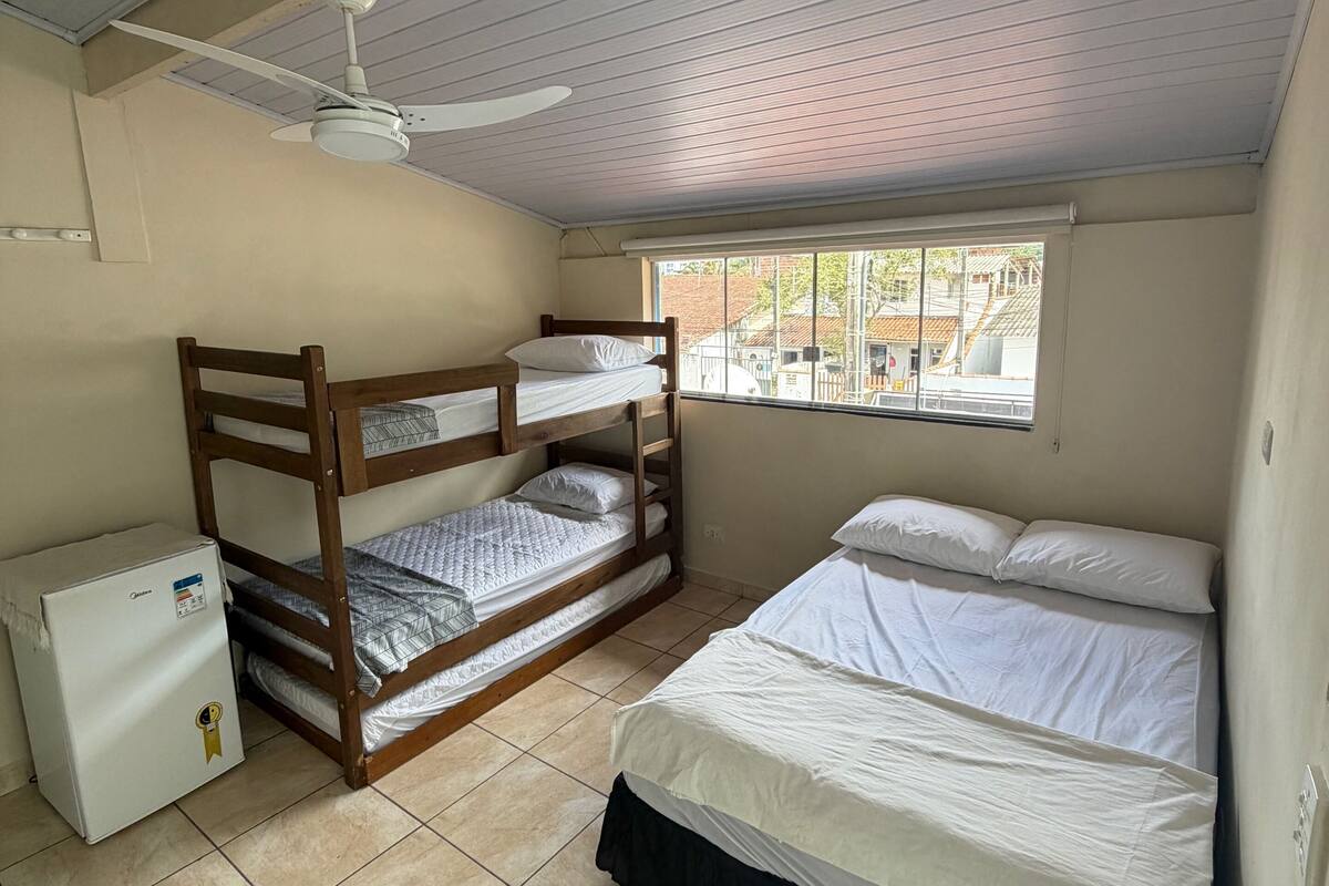 A room with a bunk bed, a single bed, a ceiling fan, a window with a view, and a refrigerator.