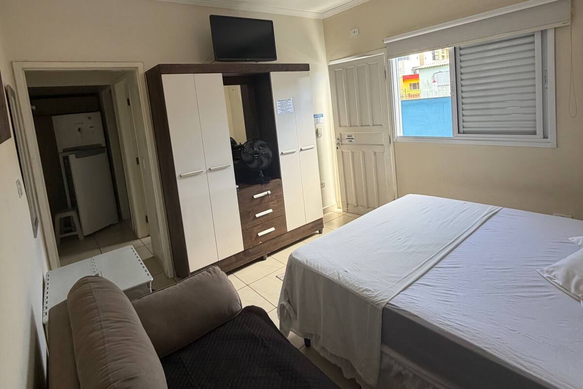 A bedroom with a bed, a sofa, a wardrobe, and a ceiling fan.