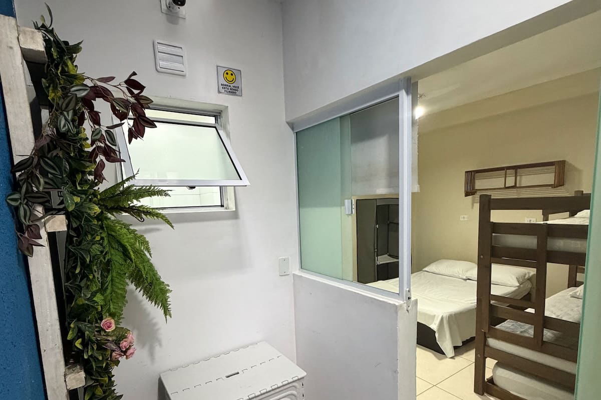 A room with a window, a small table, a bunk bed, and a door leading to another room.