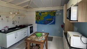 A compact kitchen with a dining table, a ceiling fan, a microwave, and a map of Brazil on the wall. - Suites Família Otaviano  (Ubatuba)