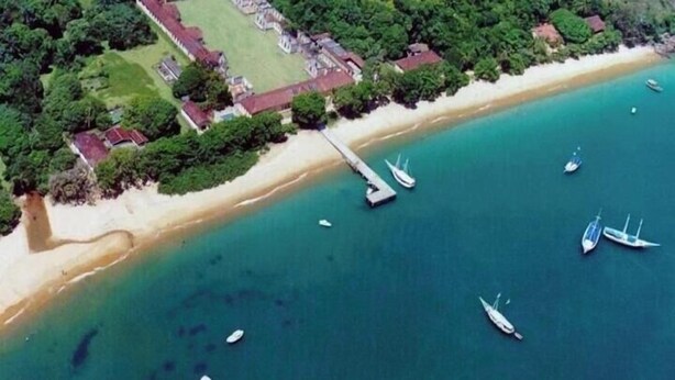 An aerial view of a coastal area with a beach, boats, and a building complex. - Suites Família Otaviano  (Ubatuba)