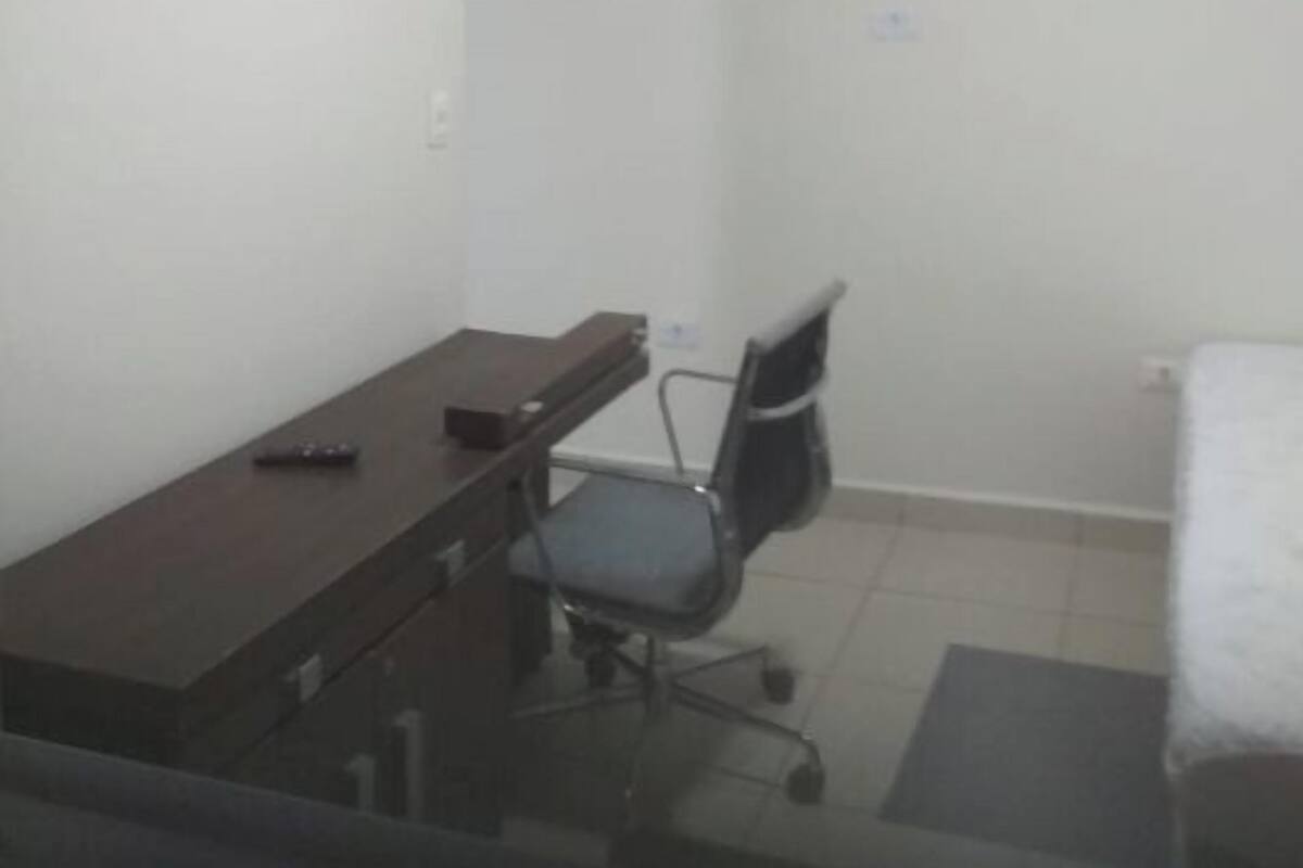 A small, sparsely furnished room with a desk, chair, and a mounted television.