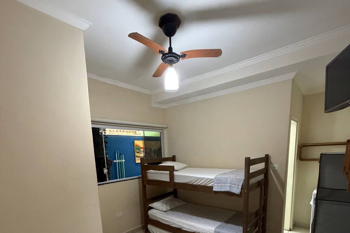 A room with bunk beds, a ceiling fan, a window with a view, and a desk.