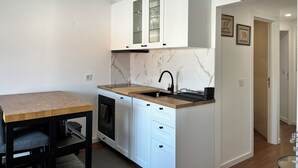 Cocina compacta con armarios blancos, salpicadero de mármol, horno empotrado y mesa de comedor de madera.