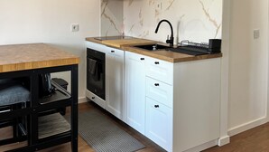 Cocina compacta con muebles blancos, encimera de madera, grifo negro y salpicadero de mármol.