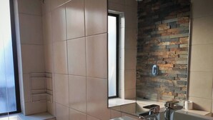 Een moderne badkamer met een grote spiegel, een douche, een wastafel en een toilet.