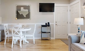 Ein Zimmer mit einem weißen Tisch und Stühlen, einem schwarzen Fernseher an der Wand, einer Tür und einer Lampe.