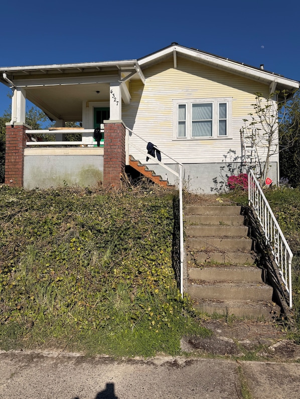A two-story house with a covered porch, a brick chimney, and a staircase leading to the front door.