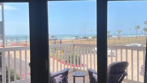 Un balcón con vista a la playa y al océano, una mesa y dos sillas.
