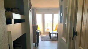 Un pasillo estrecho con suelo de madera, una puerta a la derecha y un banco al fondo.