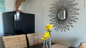 Ein Essbereich mit einem schwarzen Tisch, gewobenen Stühlen, einer Vase mit gelben Blumen, einem dekorativen Spiegel und einer Fischskulptur an der Wand.