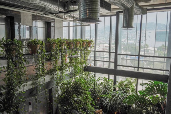 Ein mehrgeschossiges Atrium mit hängenden Pflanzen und großen Fenstern, die einen Blick auf die Stadt ermöglichen.