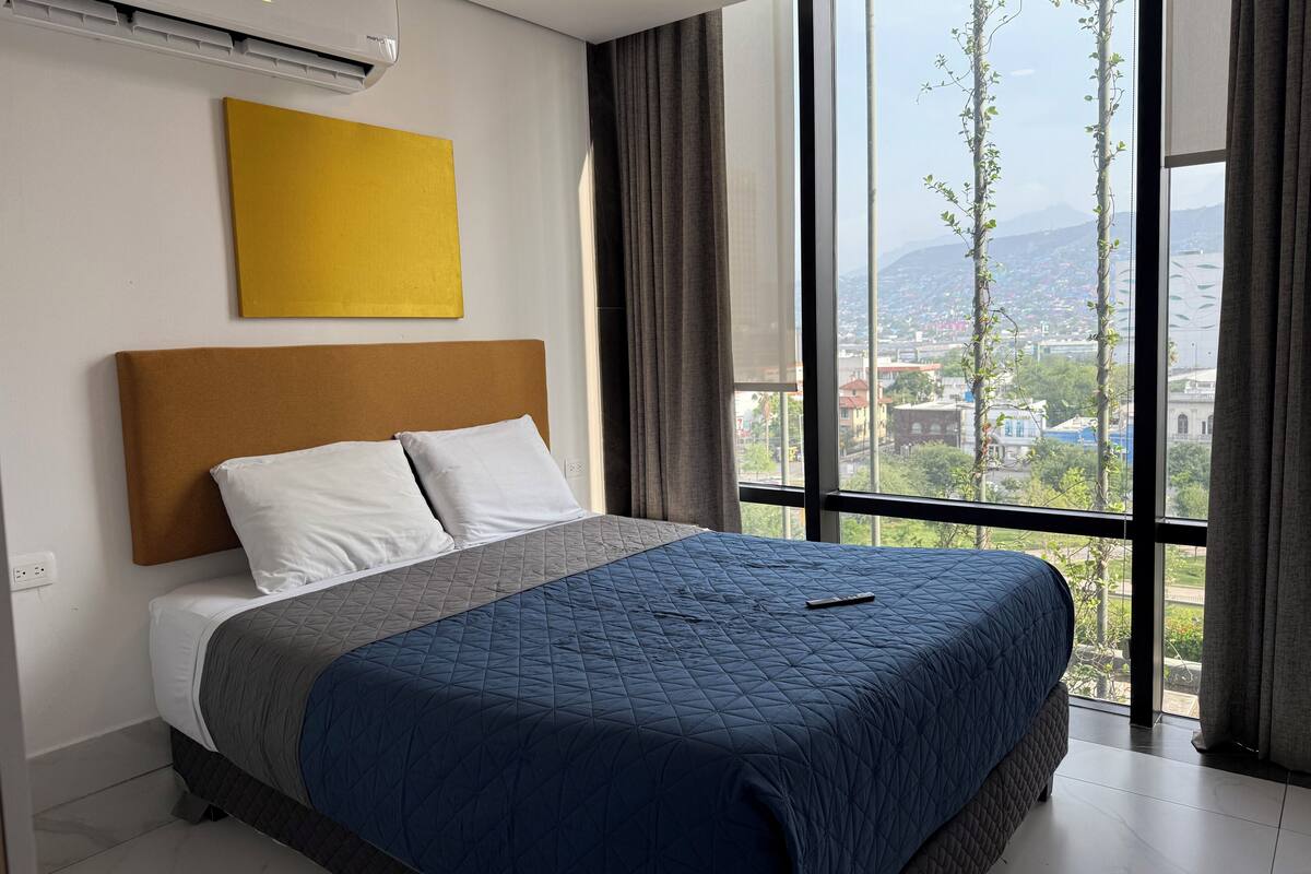 Quarto de hotel com uma cama grande, vista para o horizonte urbano e aparelho de ar condicionado.