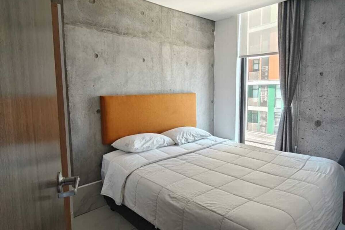 Quarto de hotel moderno com uma cama grande, paredes de concreto e vista da cidade.