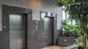 Un ascensor moderno con detalles metálicos, una pared de concreto y piso de madera.
