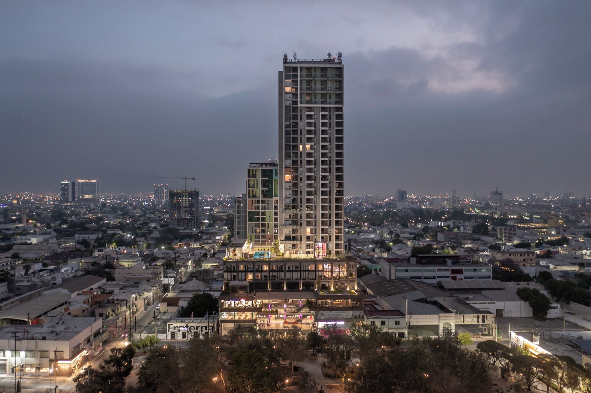 Un edifici alt amb nombrosos pisos, envoltat d'un paisatge urbà a la posta de sol.