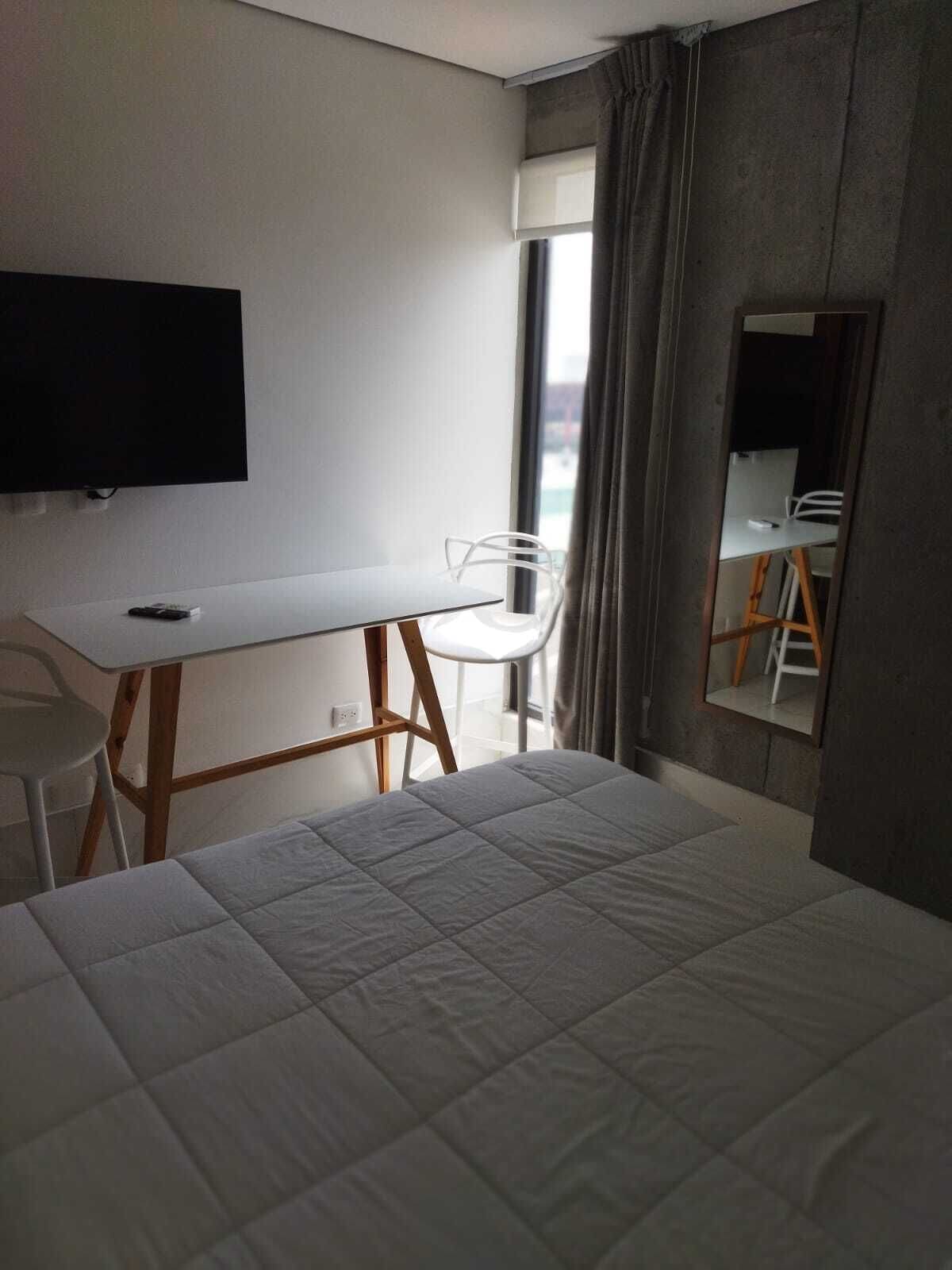 A hotel room with a bed, a desk, a chair, a TV, and a window with curtains.