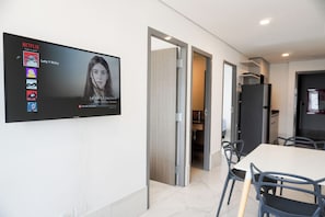A modern room with a flat-screen TV displaying a Netflix interface, a dining table with chairs, and a kitchen area visible through an open door. - Purísima 5.0 (Monterrey)