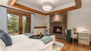 Un dormitorio con cama, escritorio, chimenea y vistas al exterior.