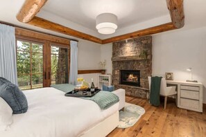 A bedroom with a bed, a desk, a fireplace, and a view of the outdoors. - Abode at Timber Ridge, ski-in/out luxury home (Teton Village)