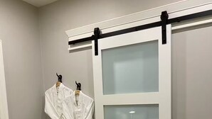 Ein Schlafzimmer mit einem Bett, einer grünen Tagesdecke, einer Schiebetür und zwei weißen Bademänteln, die an Haken hängen.