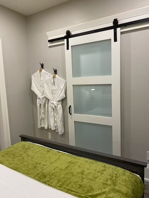 Ein Schlafzimmer mit einem Bett, einer grünen Tagesdecke, einer Schiebetür und zwei weißen Bademänteln, die an Haken hängen.