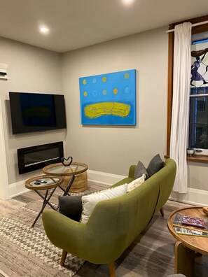 A living room with a green sofa, a flat-screen TV, a fireplace, and a painting on the wall.