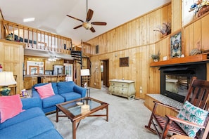 A wooden interior with a sofa, coffee table, fireplace, and a kitchen area. - Thistle: Semi-Oceanfront home in Duck, Elevator, Sanderling Community Amenities (Duck)