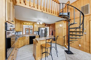 A kitchen with wooden cabinets, a stainless steel refrigerator, a built-in oven, and a black metal spiral staircase.