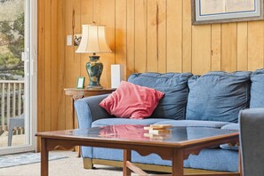 A room with a blue sofa, a wooden table, a lamp, and a framed picture on the wall. - Thistle: Semi-Oceanfront home in Duck, Elevator, Sanderling Community Amenities (Duck)