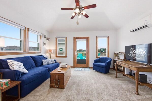 A living room with a blue sofa, a wooden coffee table, a TV, and a ceiling fan. - Thistle: Semi-Oceanfront home in Duck, Elevator, Sanderling Community Amenities (Duck)