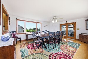 A dining area with a wooden table and chairs, a ceiling fan, and large windows.