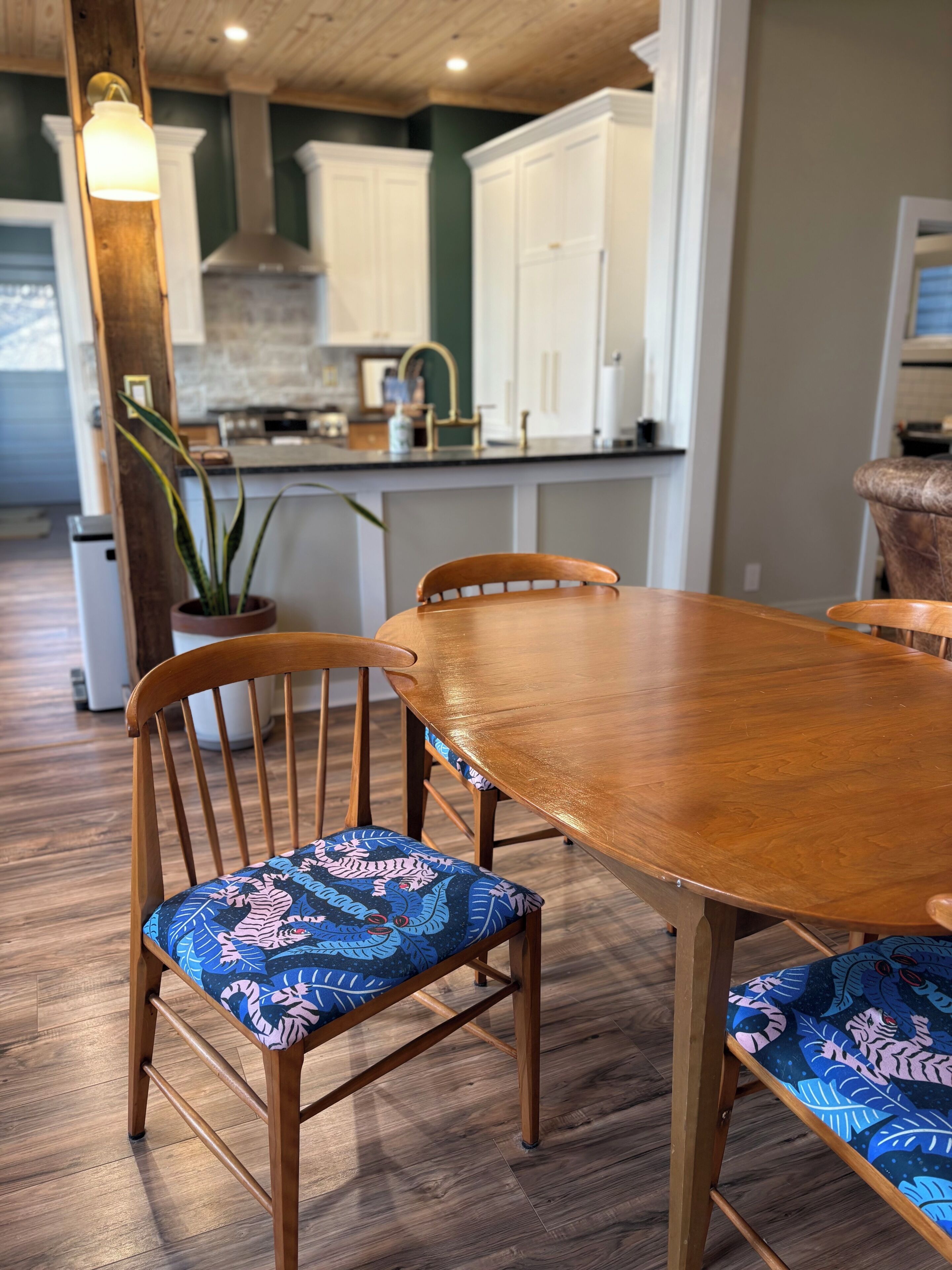 Une table à manger en bois, avec des chaises, une plante en pot et une cuisine en arrière-plan.
