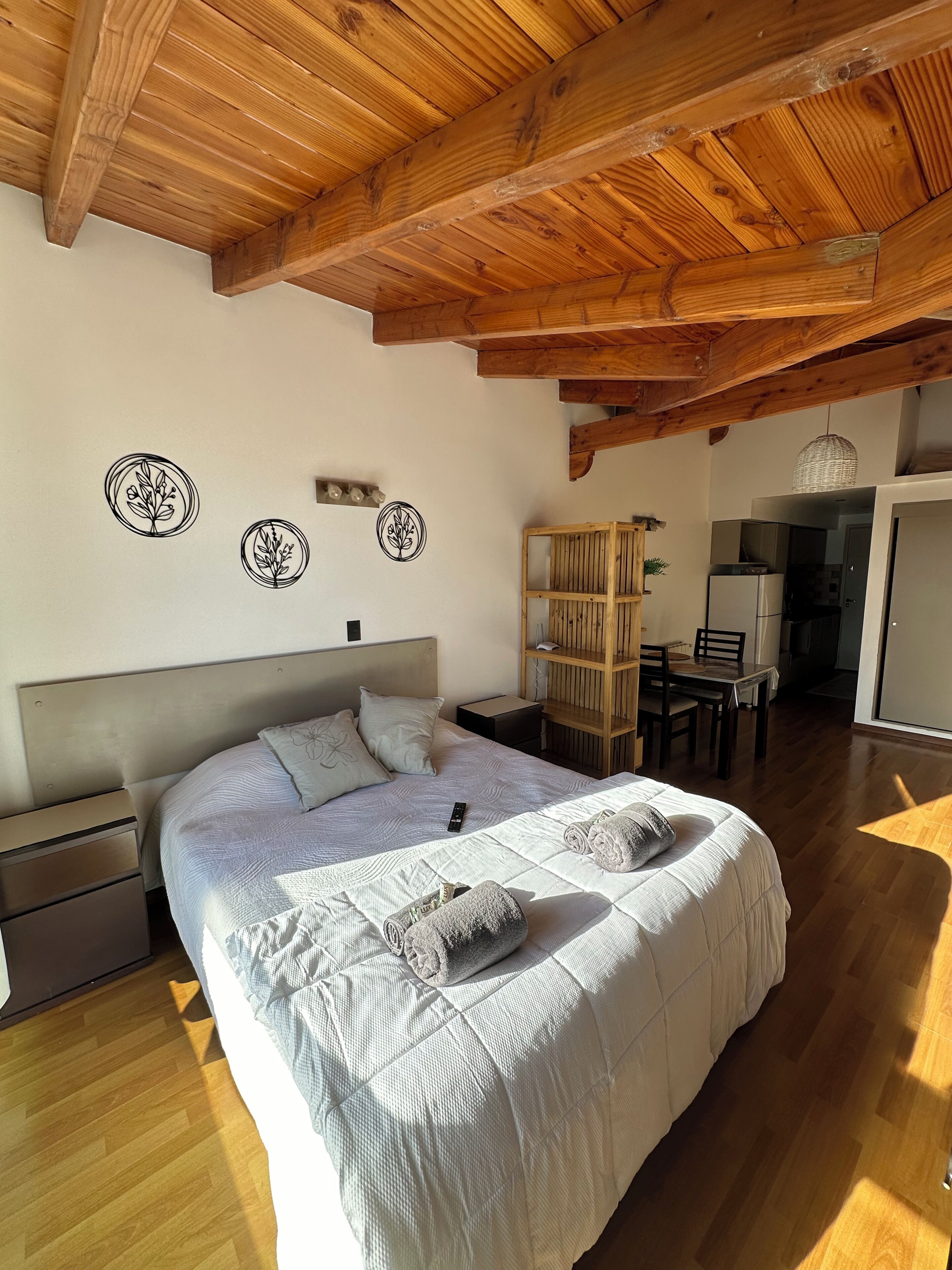 A bedroom with a wooden ceiling, a bed with pillows, a bedside table, and a small desk with a chair.