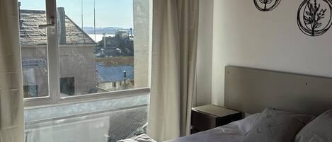 A bedroom with a large window, a bed with rolled towels, a nightstand, and wall art.