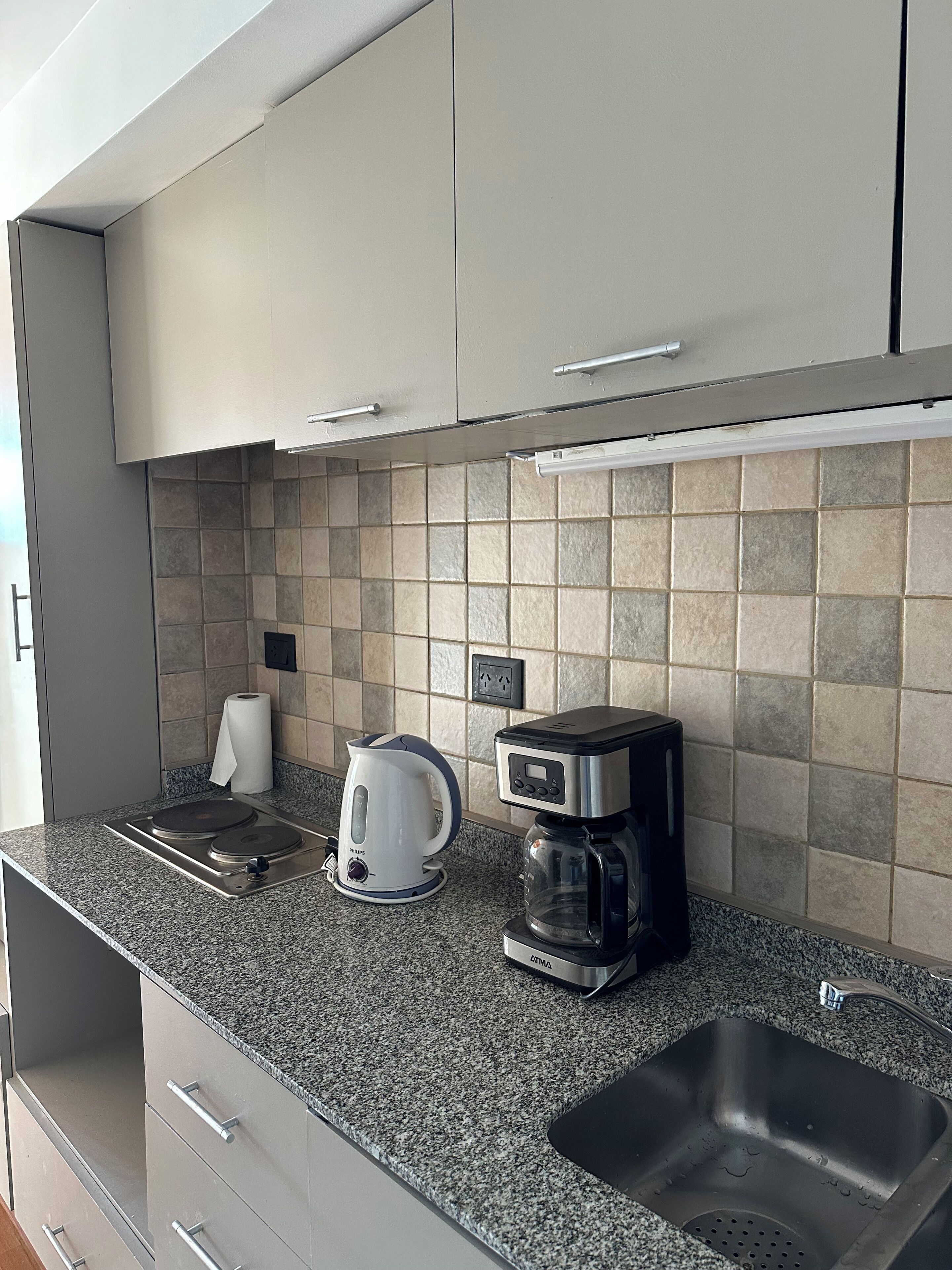 A modern kitchen with a built-in stove, a kettle, a coffee maker, and a stainless steel sink.