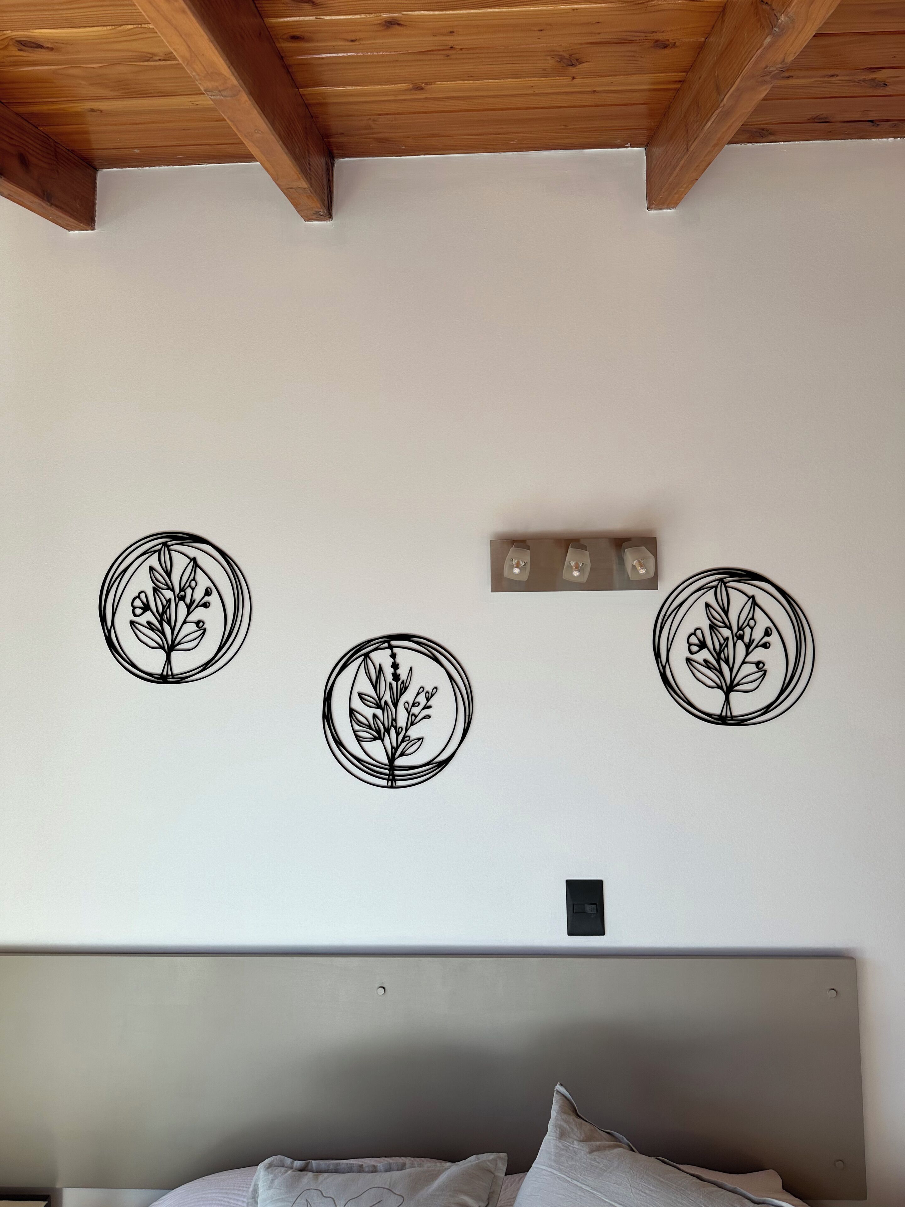 Une chambre avec un plafond en bois, un lit doté d’une tête de lit grise et trois appliques murales.