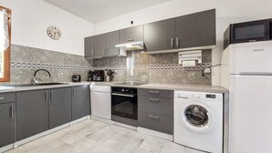 Una cucina compatta con mobili grigi, lavastoviglie, lavatrice, forno integrato e microonde.