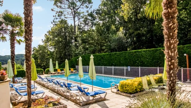 Area piscina con lettini e ombrelloni, immersa nel verde e delimitata da una recinzione.