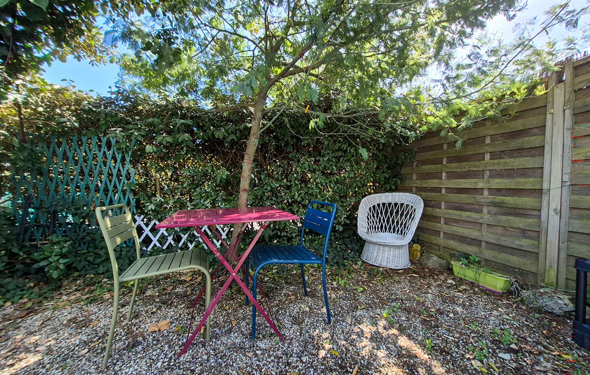 Une terrasse avec une table et des chaises, entourée d’une clôture en bois et d’un feuillage dense.